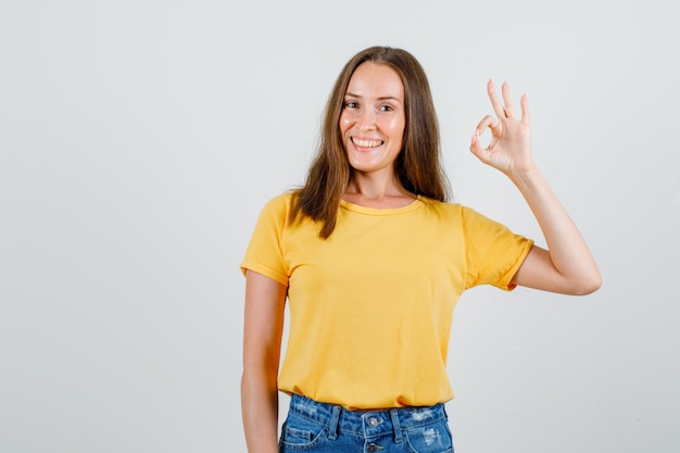 Giovane donna in maglietta, pantaloncini che mostrano segno giusto e che sembrano allegri