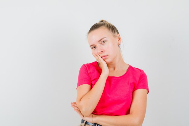 Giovane donna in maglietta rosa che si appoggia sulla guancia sul palmo e che sembra calma