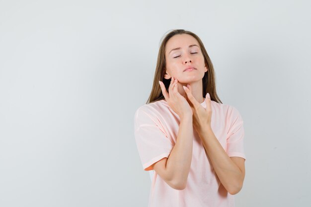 Giovane donna in maglietta rosa che tocca la pelle sul collo e sul mento e sembra affascinante.