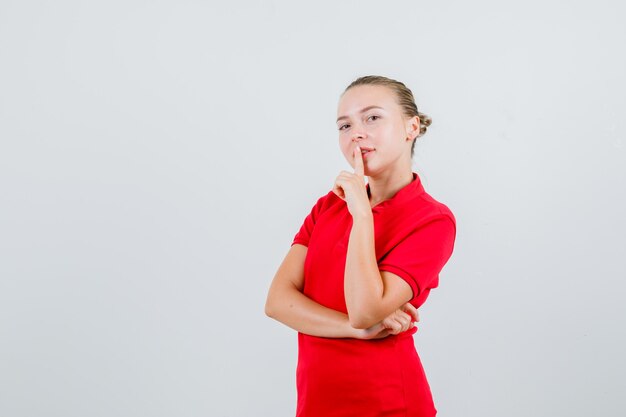 Giovane donna in maglietta rossa che mostra gesto di silenzio e guardando attento