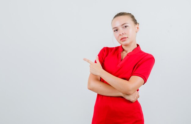 Giovane donna in maglietta rossa che punta al lato e che sembra sicura