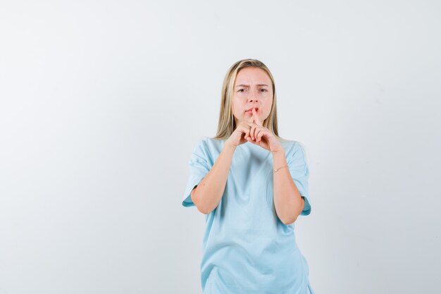 Giovane donna in maglietta tenendo le dita sulla bocca e guardando serio, vista frontale.