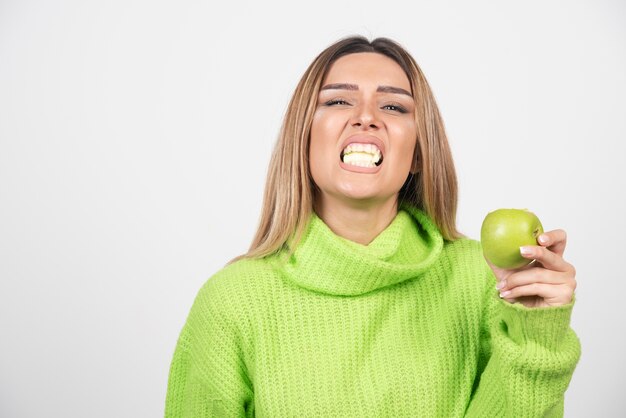 Giovane donna in maglietta verde che mangia una mela.