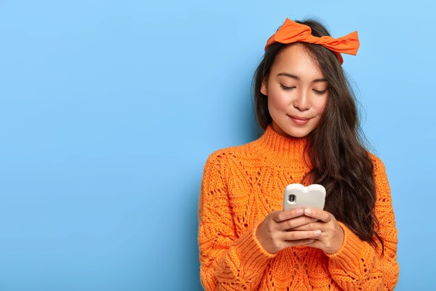 Giovane donna in maglione arancione in chat sul suo smartphone
