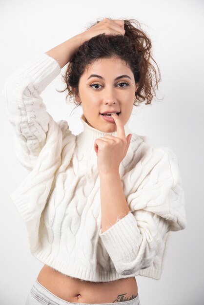 Giovane donna in maglione bianco in piedi su un muro bianco. Foto di alta qualità