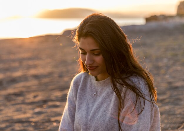 Giovane donna in maglione che si siede sulla riva del mare