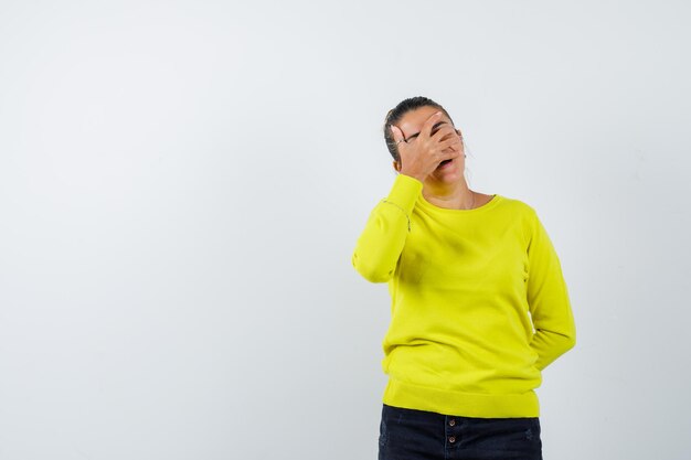Giovane donna in maglione giallo e pantaloni neri che copre il viso con la mano e sembra tormentata