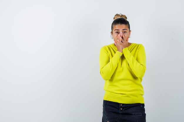 Giovane donna in maglione, gonna di jeans che copre il viso con la mano e sembra stupita