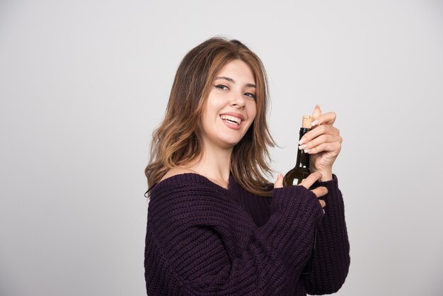 Giovane donna in maglione lavorato a maglia caldo che tiene una bottiglia di vino.