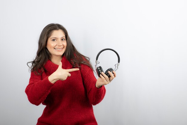 Giovane donna in maglione rosso che punta alle cuffie.