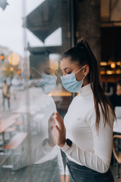 Giovane donna in maschera per il viso in piedi davanti alle finestre nella caffetteria