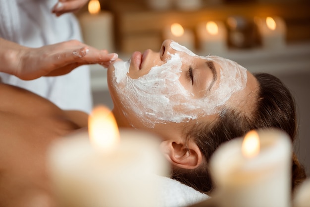 Giovane donna in maschera per viso rilassante nel salone spa.