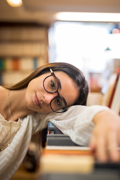 Giovane donna in occhiali pendente testa su libri in libreria