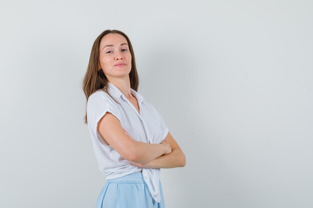 Giovane donna in piedi con le braccia incrociate in camicetta e gonna e guardando fiducioso