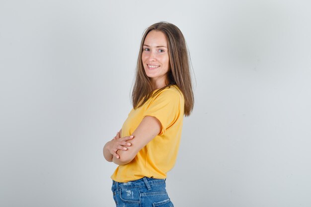 Giovane donna in piedi con le braccia incrociate in t-shirt, pantaloncini e guardando allegro