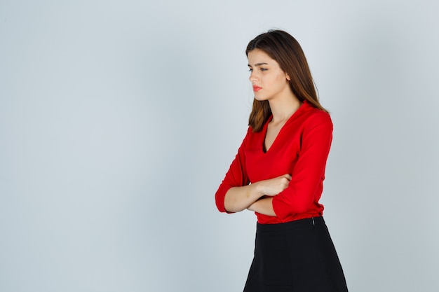 Giovane donna in piedi con le braccia incrociate mentre guarda lontano in camicetta rossa