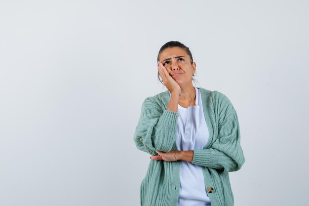 Giovane donna in piedi in posa di pensiero in camicia bianca e cardigan verde menta e guardando pensierosa