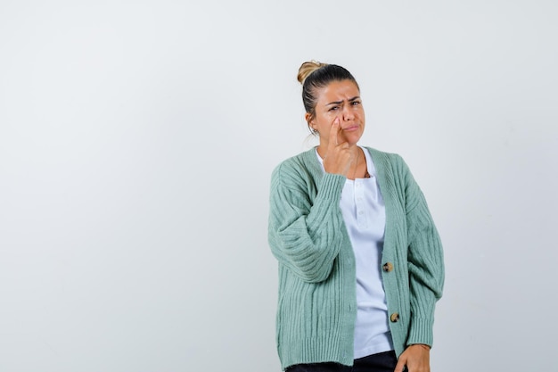 Giovane donna in piedi in posa di pensiero in camicia bianca e cardigan verde menta e guardando pensierosa