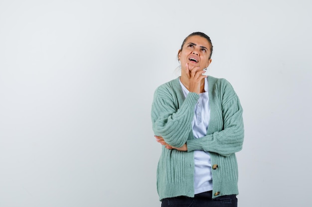 Giovane donna in piedi in posa di pensiero in camicia bianca e cardigan verde menta e sembra felice