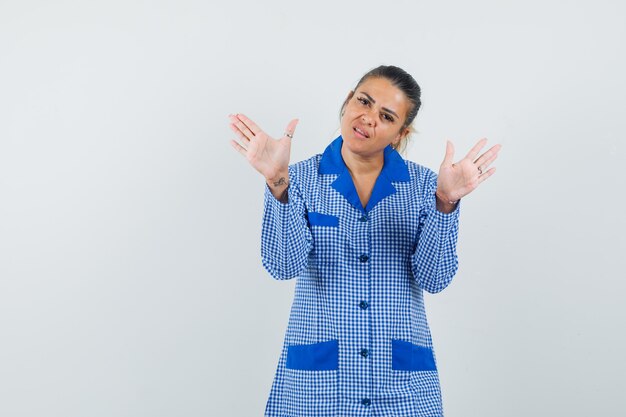 Giovane donna in piedi in posa di resa in camicia pigiama a quadretti blu e sembra carina. vista frontale.