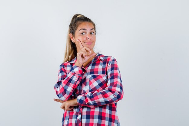 Giovane donna in piedi nel pensiero pongono in camicia casual e sembra ragionevole, vista frontale.