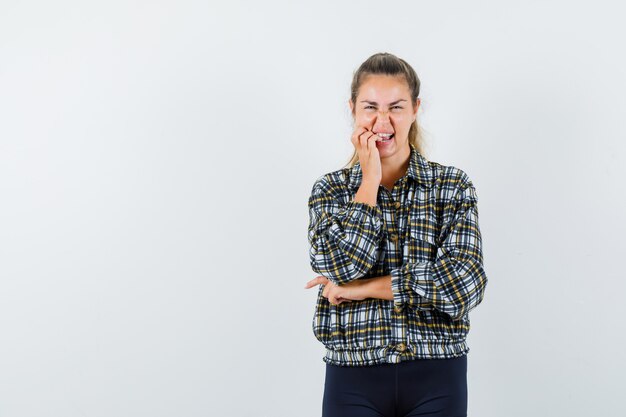 Giovane donna in piedi nel pensiero pongono in camicia, pantaloncini e sembra felice, vista frontale.