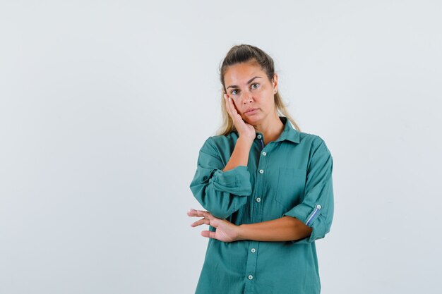 Giovane donna in piedi nel pensiero posa in camicetta verde e guardando pensieroso