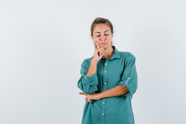 Giovane donna in piedi nel pensiero posa in camicetta verde e guardando pensieroso