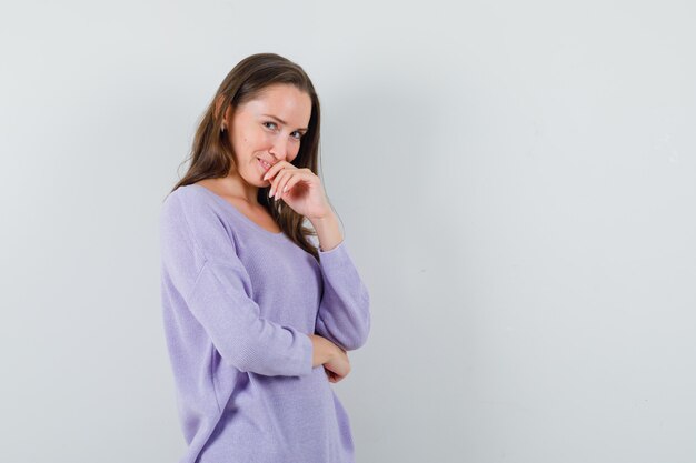 Giovane donna in piedi nel pensiero posa in camicia casual e sembra allegra