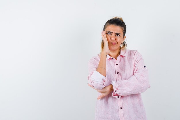 Giovane donna in piedi nel pensiero posa in camicia rosa e guardando indeciso