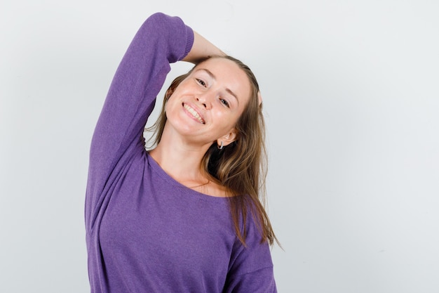 Giovane donna in posa con la mano sulla testa in camicia viola e guardando affascinante, vista frontale.