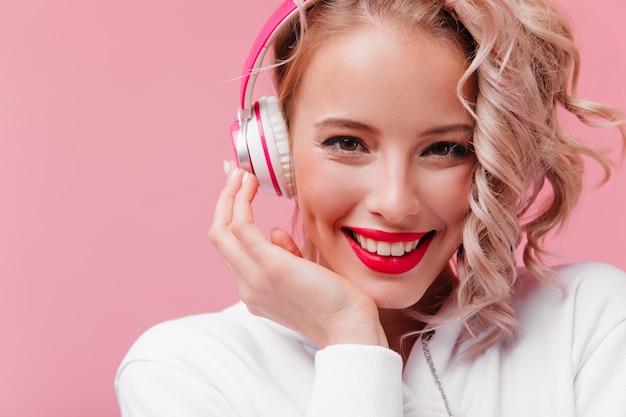 Giovane donna in posa e ascolta la musica attraverso le sue cuffie rosa
