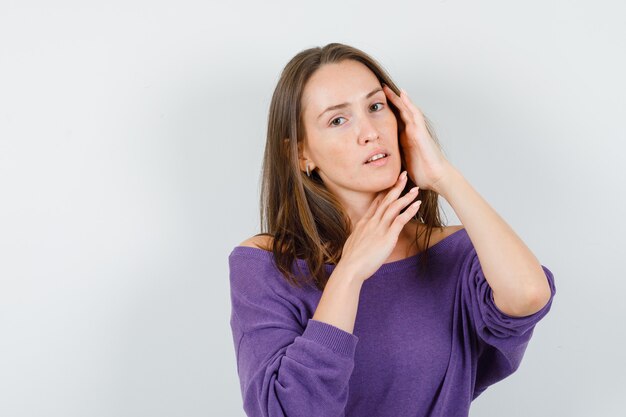 Giovane donna in posa mentre guarda la telecamera in camicia viola e sembra elegante, vista frontale.