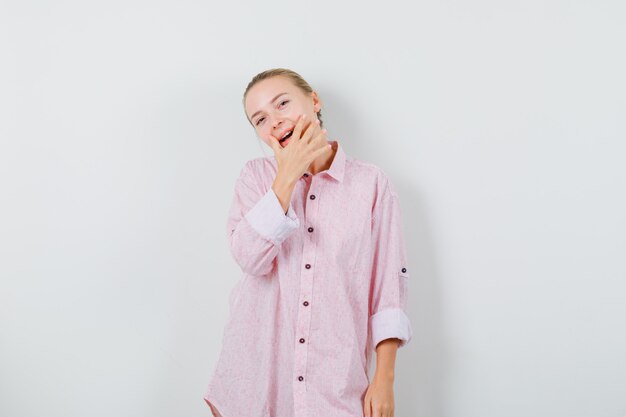 Giovane donna in posa mentre in piedi in camicia rosa e sembra allegra