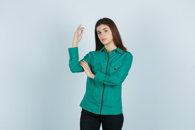 Giovane donna in posa mentre si alza la mano in camicia verde, pantaloni e sembra bellissima. vista frontale.