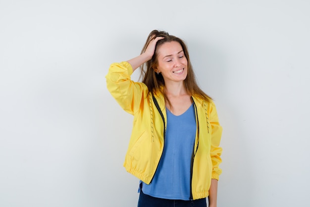 Giovane donna in posa mentre si pettina i capelli con la mano in maglietta, giacca e guarda le vertigini, vista frontale.