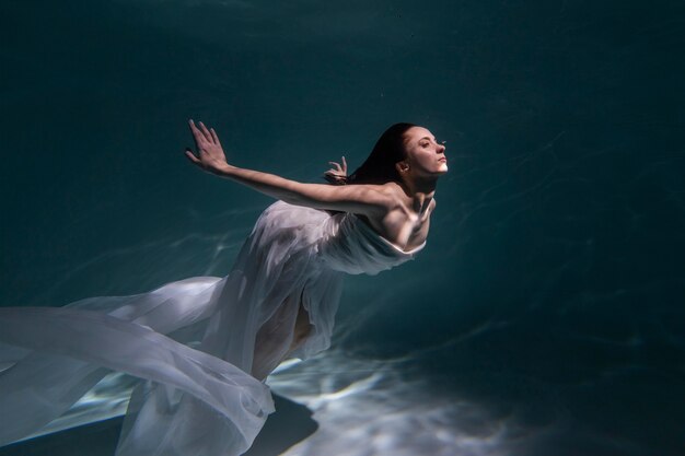 Giovane donna in posa sommersa sott'acqua in un vestito fluido