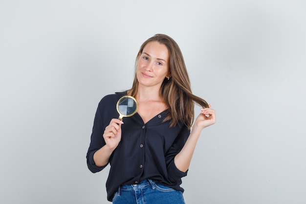 Giovane donna in posa tenendo i capelli con la lente d'ingrandimento in camicia nera