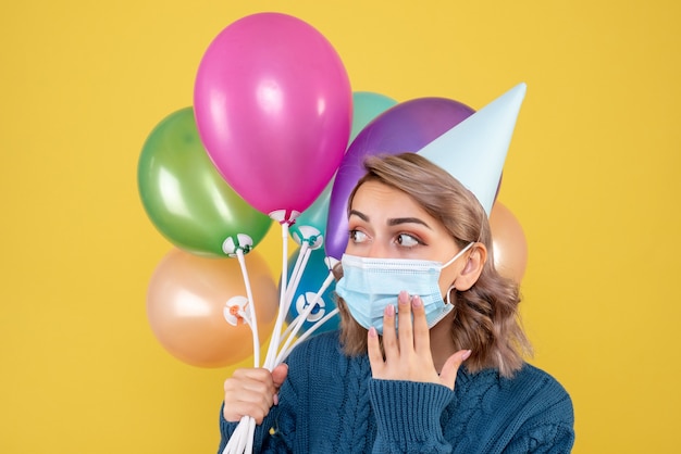 giovane donna in possesso di palloncini colorati in maschera sul giallo