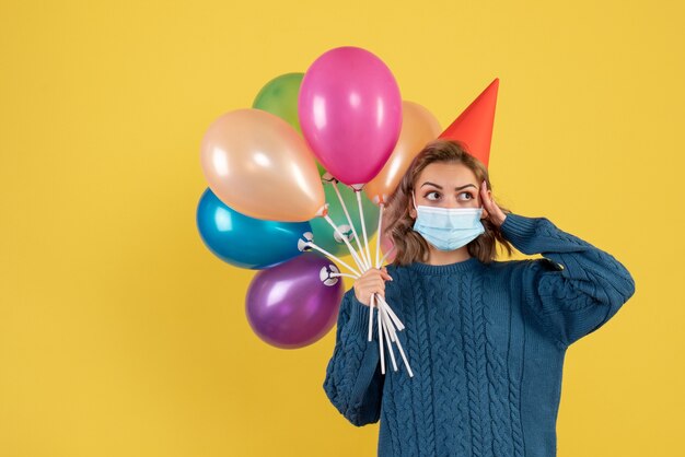 giovane donna in possesso di palloncini colorati in maschera sul giallo