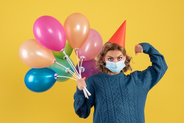 giovane donna in possesso di palloncini colorati su giallo