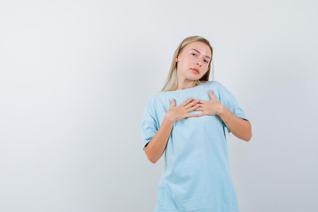 Giovane donna in t-shirt che mostra mano nella mano sul petto e sembra speranzosa