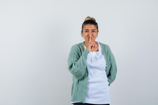 Giovane donna in t-shirt, giacca che mostra gesto di silenzio e sembra felice