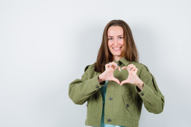 Giovane donna in t-shirt, giacca che mostra il gesto del cuore e sembra carina, vista frontale.