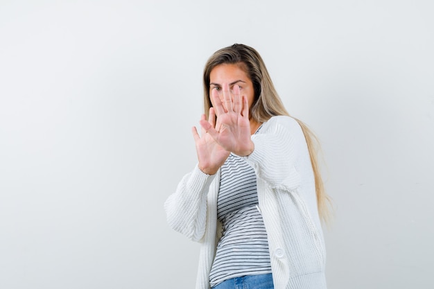 Giovane donna in t-shirt, giacca che mostra il gesto di arresto e sembra spaventata, vista frontale.