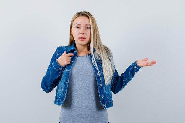 Giovane donna in t-shirt, giacca di jeans, gonna che allunga la mano in un gesto interrogativo e sembra pensierosa