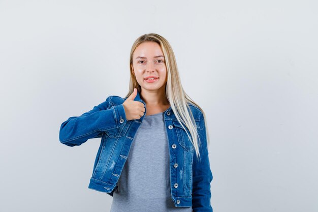 Giovane donna in t-shirt, giacca di jeans, gonna che mostra pollice in su e sembra allegra