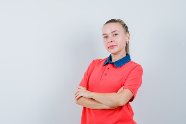 Giovane donna in t-shirt in piedi con le braccia incrociate e guardando fiducioso