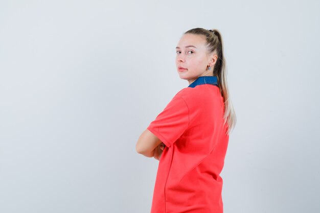 Giovane donna in t-shirt in piedi con le braccia incrociate e guardando fiducioso