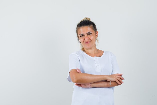 Giovane donna in t-shirt in piedi con le braccia incrociate e guardando fiducioso